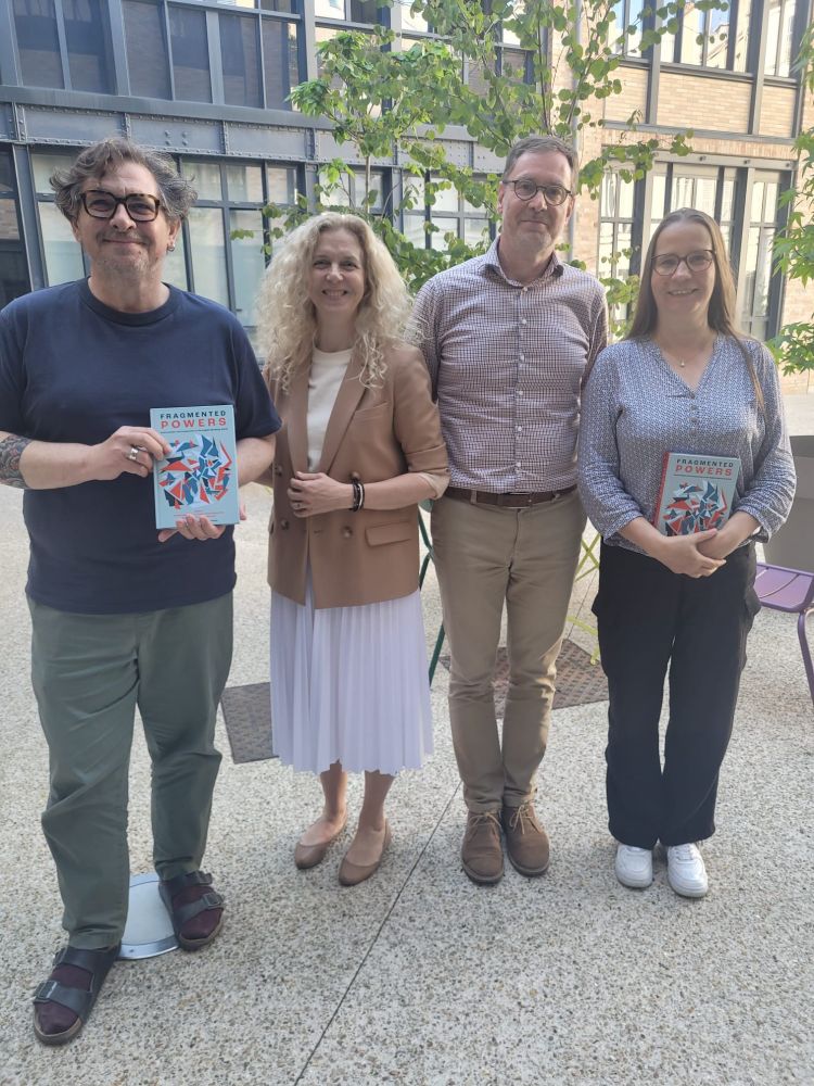 Fabrice Moulon, Laurence Cossu-Beaumont, David Fée and Emmanuelle Avril (standing left to right) from CREW research lab in the courtyard of Maison de la Recherche smiling and holding copies of Fragmented Powers book they coedited 