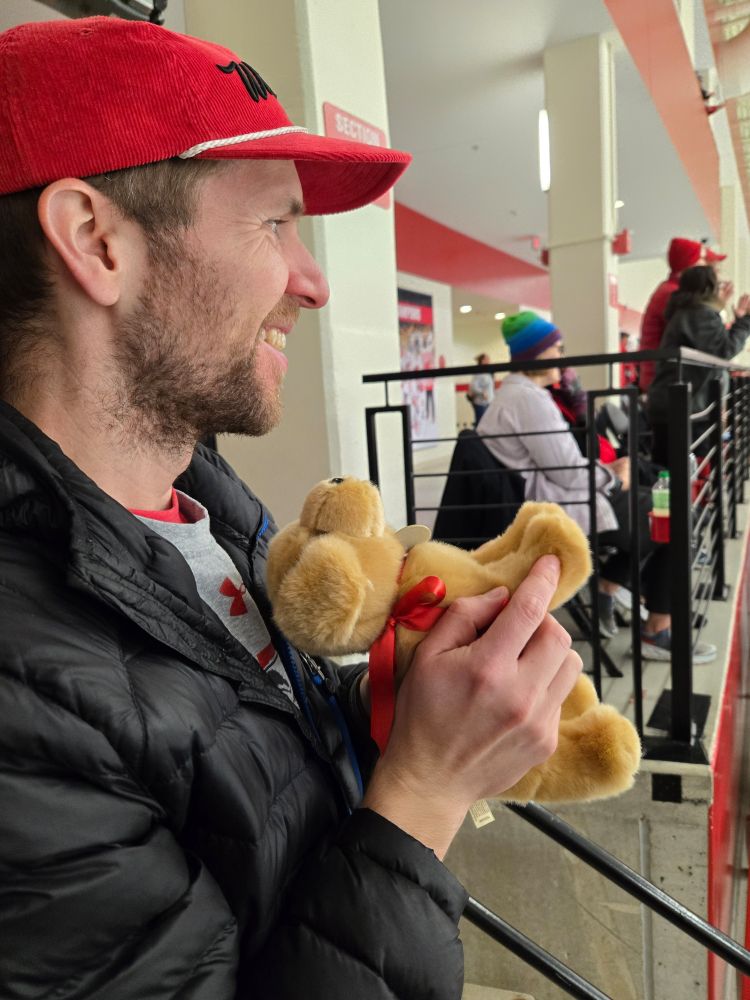 My husband holding a small stuffed puppy dog, making the paws clap together after the Badgers scored a goal. 