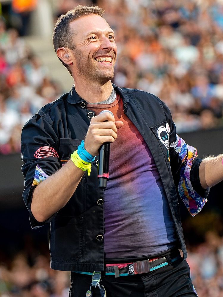 Chris Martin, vocalista do Coldplay sorrindo e segurando um microfone.