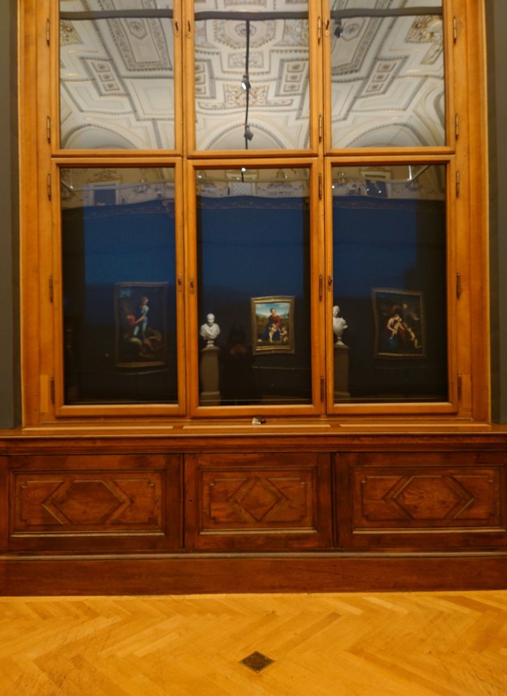 A picture of the reflections of three Raphael paintings in a wooden art gallery window. 