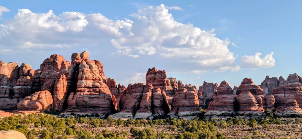 Spires of layered sandstone below blue sky and puffy white clouds. 