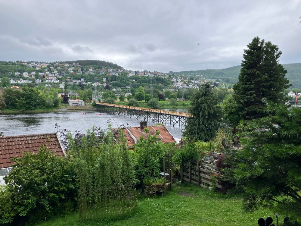 Pedestrian bridge over river. Small mountains with houses built on the mountain.