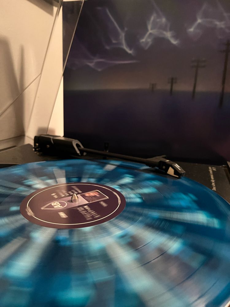 A speckled blue vinyl record spins on a turntable.  The record is “ユートピアへの旅” by desert sand feels warm at night