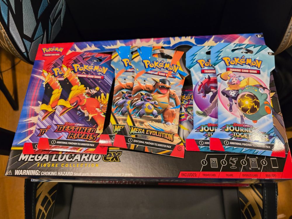 A photo of the top of the Mega Lucario ex Figure box with 6 packs on it. 2 from destined rivals, mega evolution and journey together
