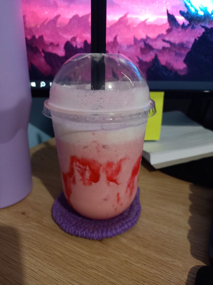 A strawberry frappe on a desk, sat on a purple coaster.
