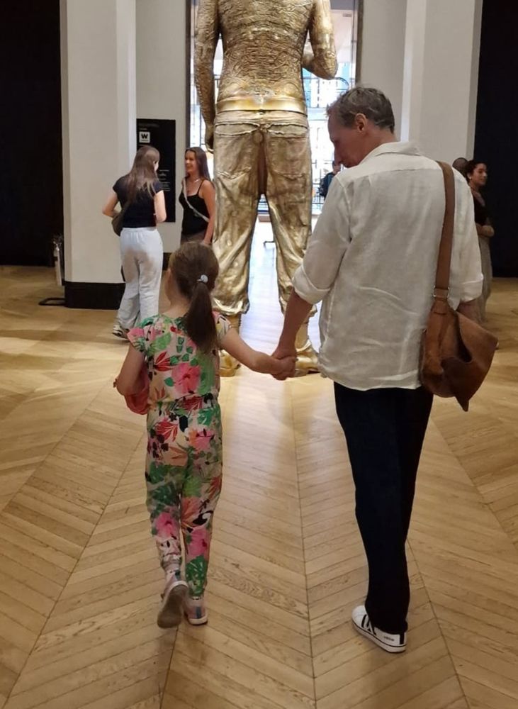a small but very noisy 7 year old girl wearing a loud outfit and her drained and worn out 50+ year old uncle holding her han,d in the London Science Museum