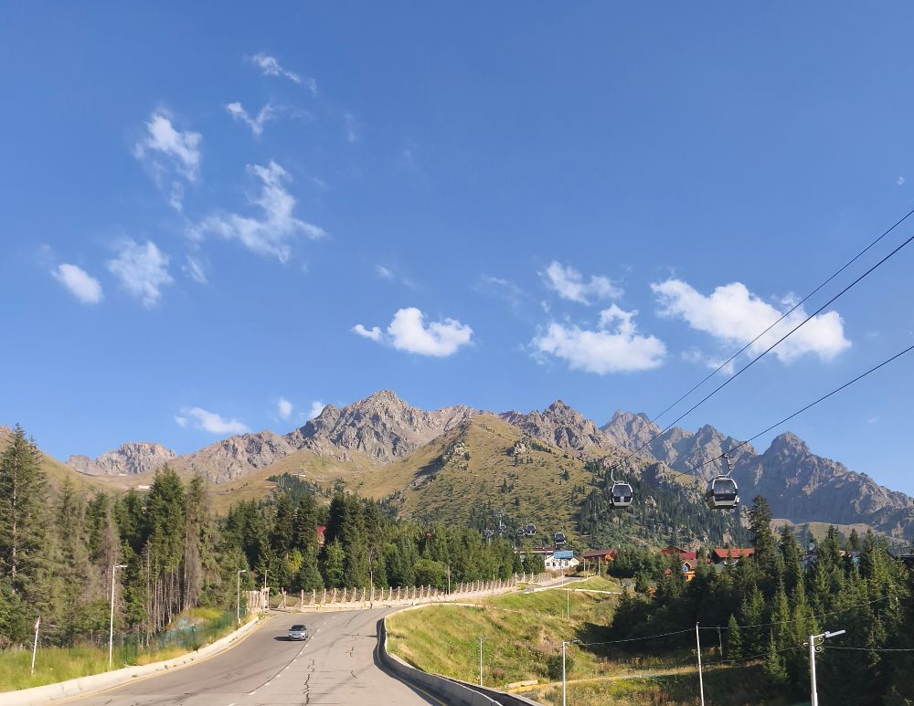 Eine Straße führt in Richtung einer kahlen Bergkette, links und rechts Bäume 