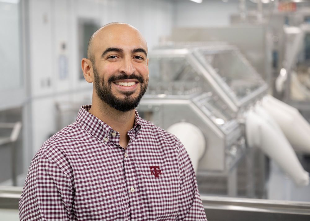 Lead Astromaterial Curation Engineer Salvador Martinez III smiles at the camera wearing a plaid shirt inside the OSIRIS REx Lab. Credit: NASA/James Blair; NASA/Thalia Patrinos