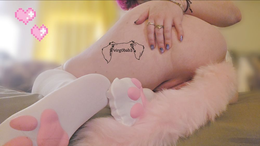 sitting on the edge of my bed on my side with my feet under me. im wearing white socks with pink 3d paw pads and a pink anal tail plug in front of them