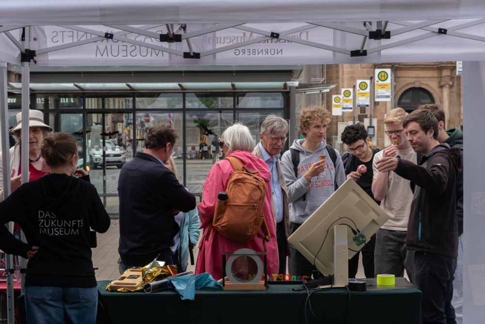 People are standing at the tent of our partner Deutsches Museum Nürnberg and getting explained the experiments there.