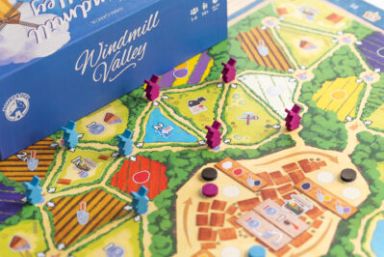 Small blue and purple wooden windmill tokens on a colourful, tulip field game board, with a box with Windmill Valley written on in the top left of the picture