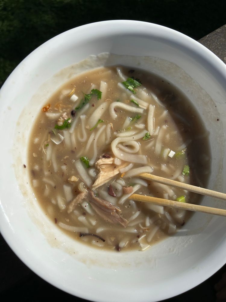 A large white bowl of khao piak, a chicken and rice noodle soup dish from Laos, with chopsticks 