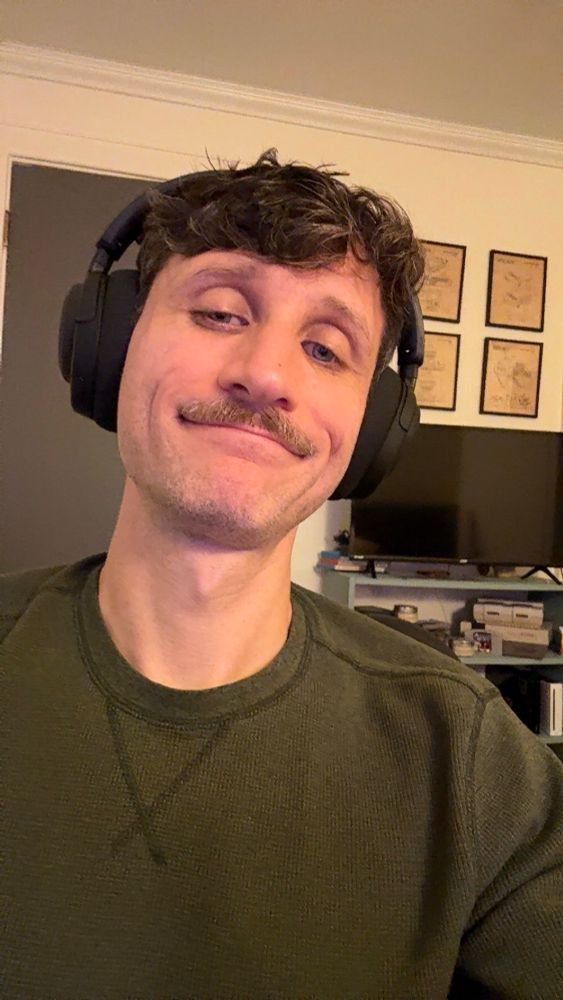 A picture of Nick in a green thermal wearing black over ear headphones. 