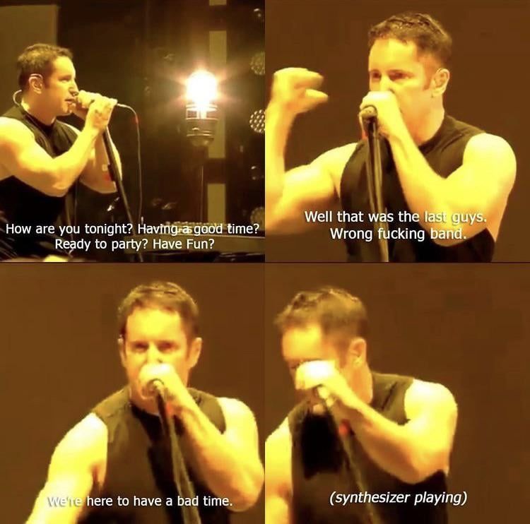 A quartet of musician Trent Reznor, headliner of the band Nine Inch Nails, on stage at a concert, dressed in a black sleeveless shirt and speaking into a microphone. He addresses the crowd in each photo. 1: "How are you tonight? Having a good time? Ready to party? Have fun?" 2: "Well that was the last guys. Wrong fucking band." 3. "We're here to have a bad time." 4. *Trent leans down to his instruments, and the caption indicates "(synthesizer playing)."