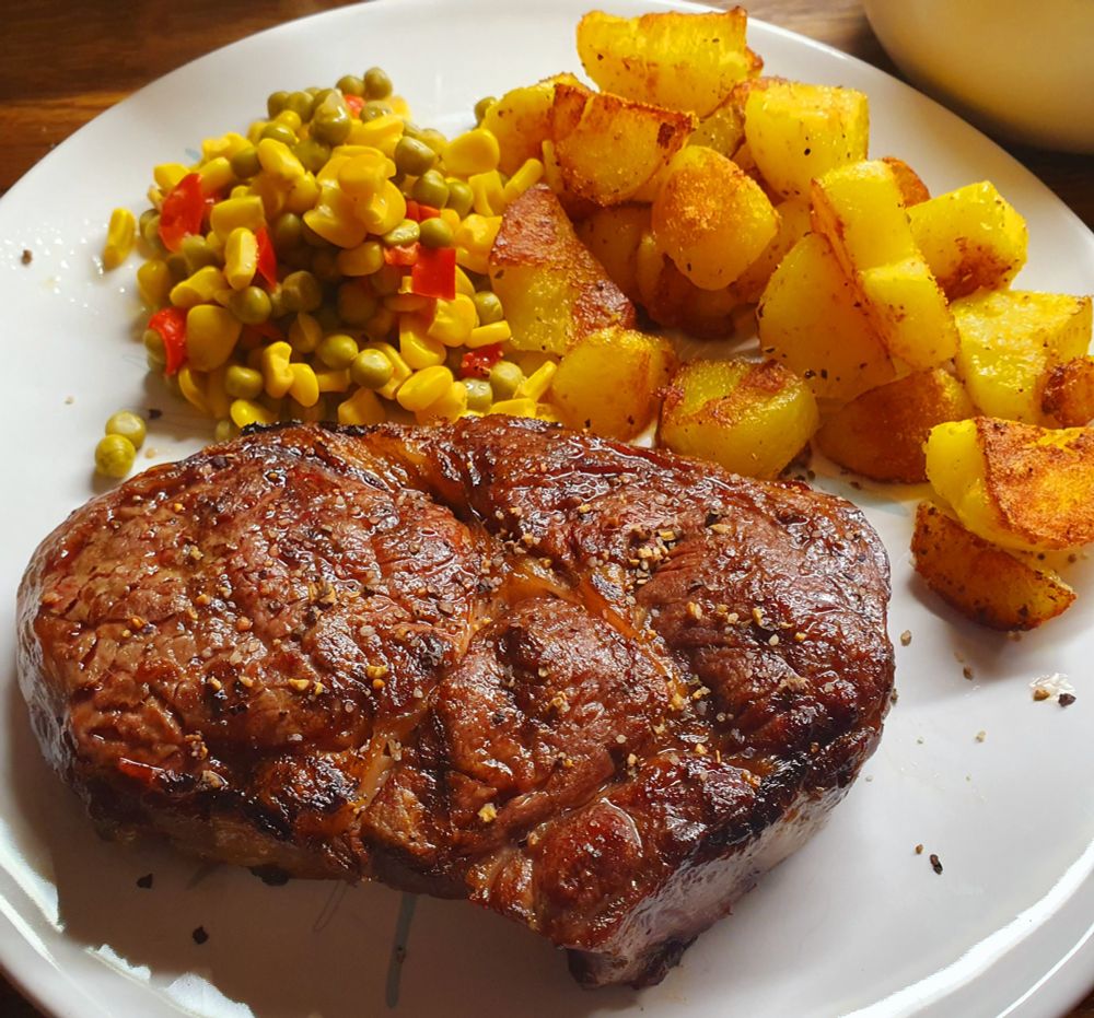 Ein gegrilltes Steak mit Bratkartoffeln und buntem Maisgemüse.