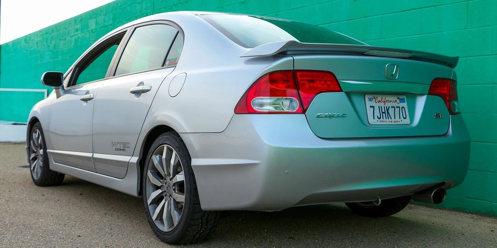 a silver car; an eighth generation honda civic si sedan. it is fairly plain looking with a modest spoiler on the back.