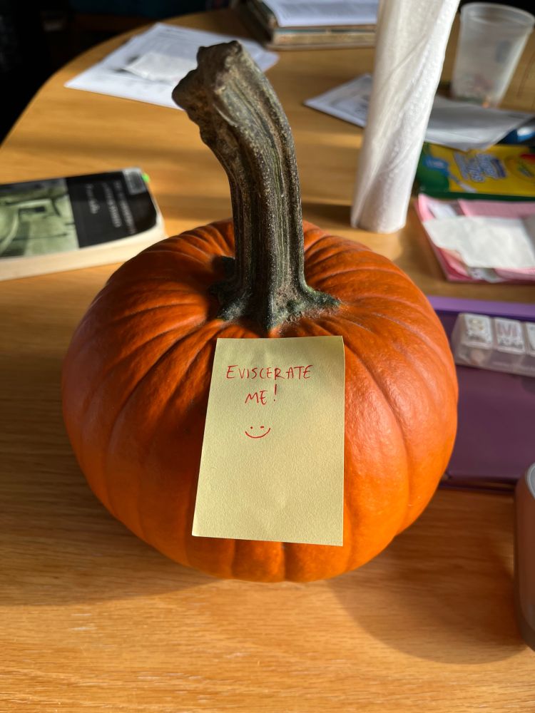 the orange pumpkin, now upon a table with a sticky note affixed to it that says "EVISCERATE ME! :)"