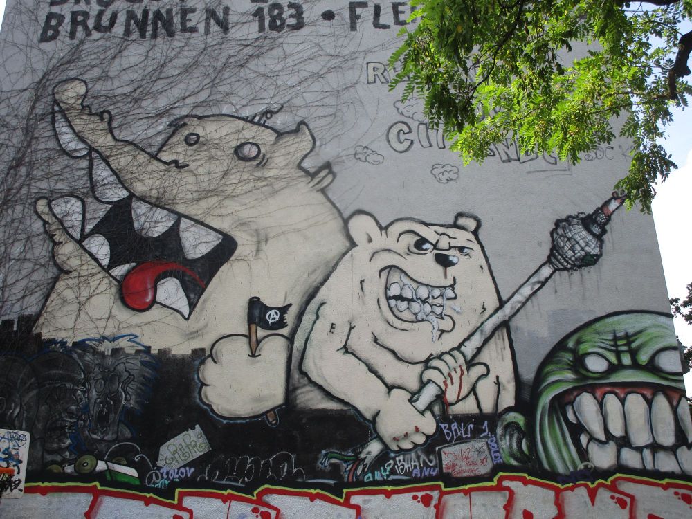Häuserwand bemalt mit grimmig schauenden Bärr und Krokodil.Der Bär hält den Berliner Fernsehturm in der Hand.