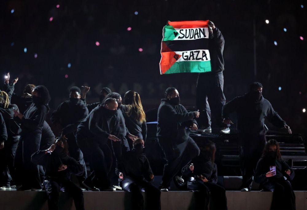 Protestor holding up a Palestinian flags. Reads “Sudan and Gaza”