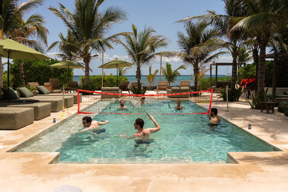 Team members playing badminton in a swimming pool near the ocean