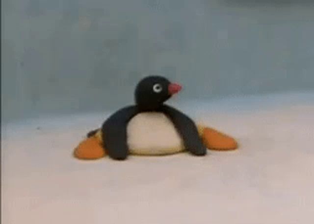 a stuffed penguin is laying on a white surface and waving .