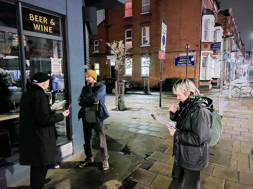Three of our volunteers standing around talking to each other holding clipboards and pens on a street corner in St Ann's Ward.