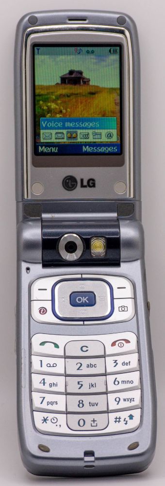 A photo of an LG L5100, flipped open displaying the main idle screen.
The wallpaper is of a house on the top of a hill, and a popup menu for calling and voicemail-related shortcuts is visible on the bottom of the screen.
