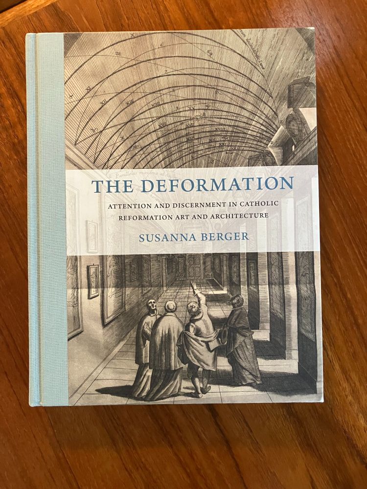 Book on a wooden table is The Deformation: Attention and Discernment in Catholic Reformation Art and Architecture, by Susanna Berger