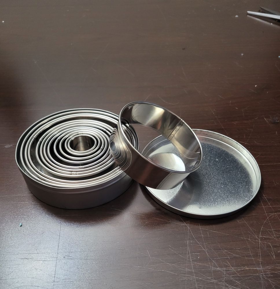 A set of aluminum circle cookie cutters sitting in their tin on a wooden work table