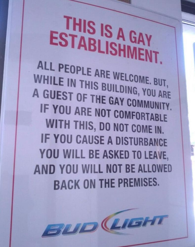 The sign reads: 

THIS IS A GAY
ESTABLISHMENT.

ALL PEOPLE ARE WELCOME. BUT,
WHILE IN THIS BUILDING, YOU ARE
A GUEST OF THE GAY COMMUNITY.
IF YOU ARE NOT COMFORTABLE
WITH THIS, DO NOT COME IN.
IF YOU CAUSE A DISTURBANCE
YOU WILL BE ASKED TO LEAVE,
AND YOU WILL NOT BE ALLOWED
BACK ON THE PREMISES.