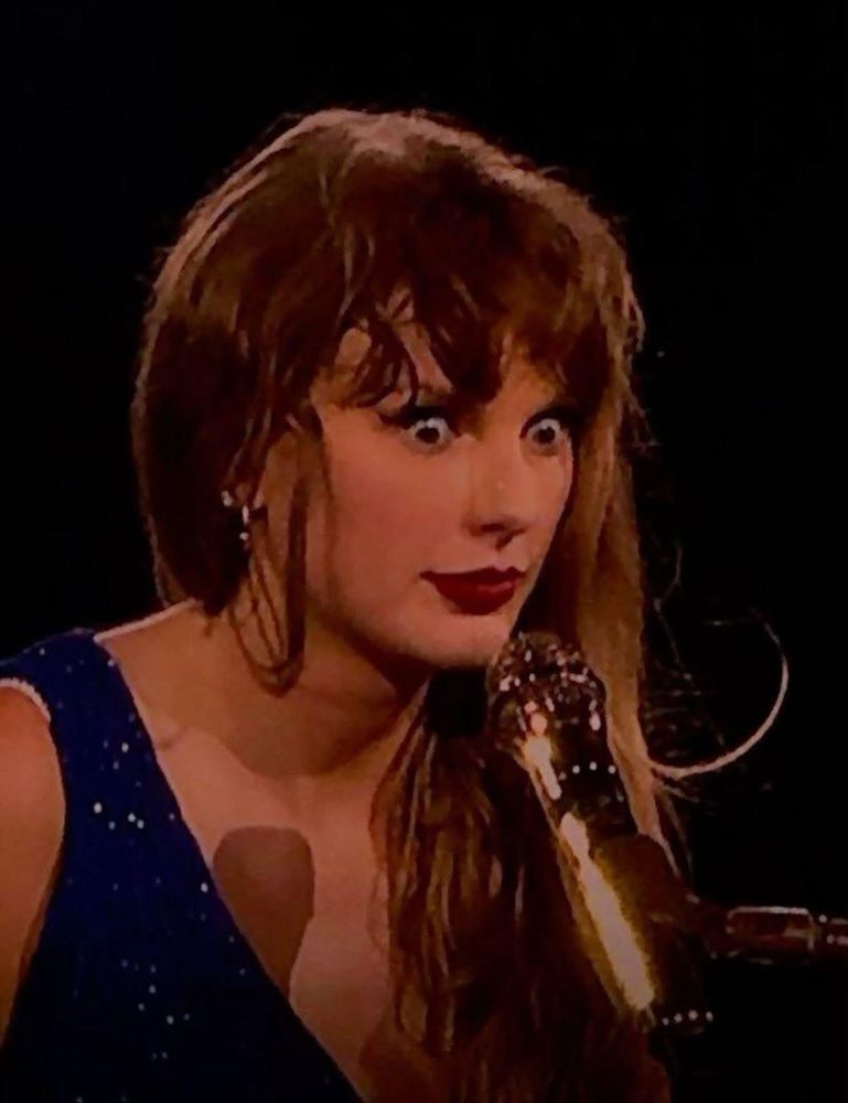 Taylor Swift pulling a face with eyes wide open and a microphone 
