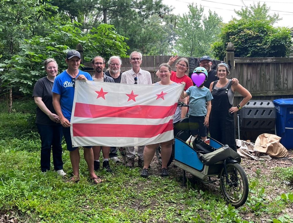 A group of people holds a DC flag in a backyard