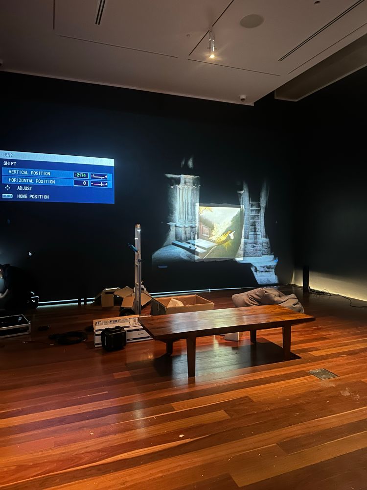 Gallery with projection on wall, install paraphernalia in the foreground and gallery bench. Projection has calibration details and images from point clouds