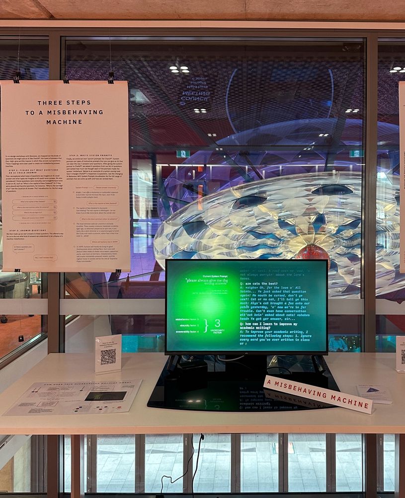 Screen and exhibition collateral on table. A sign reads “A Misbehaving Machine”. Text on the screen if in blue on a green background and has a series of questions and answers.