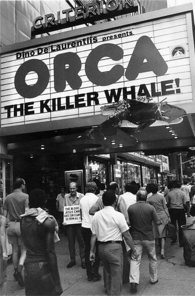 People walking on a sidewalk under the Criterion theater’s marquee in New York City, 1977, that reads “Dino De Laurentiis presents ORCA THE KILLER WHALE!”