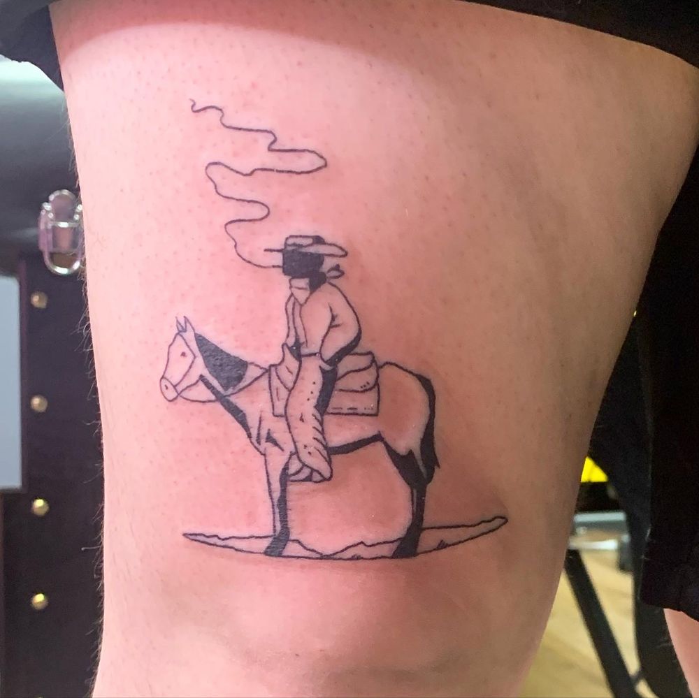 An image of a tattoo above the knee, a lone silhouetted cowboy smoking a cigarette on a horse