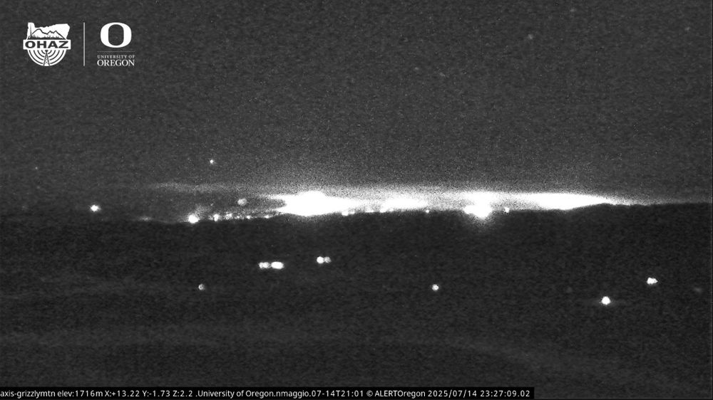 A nighttime infrared image from the Grizzly Mountain camera shows bright white fire activity on the horizon.