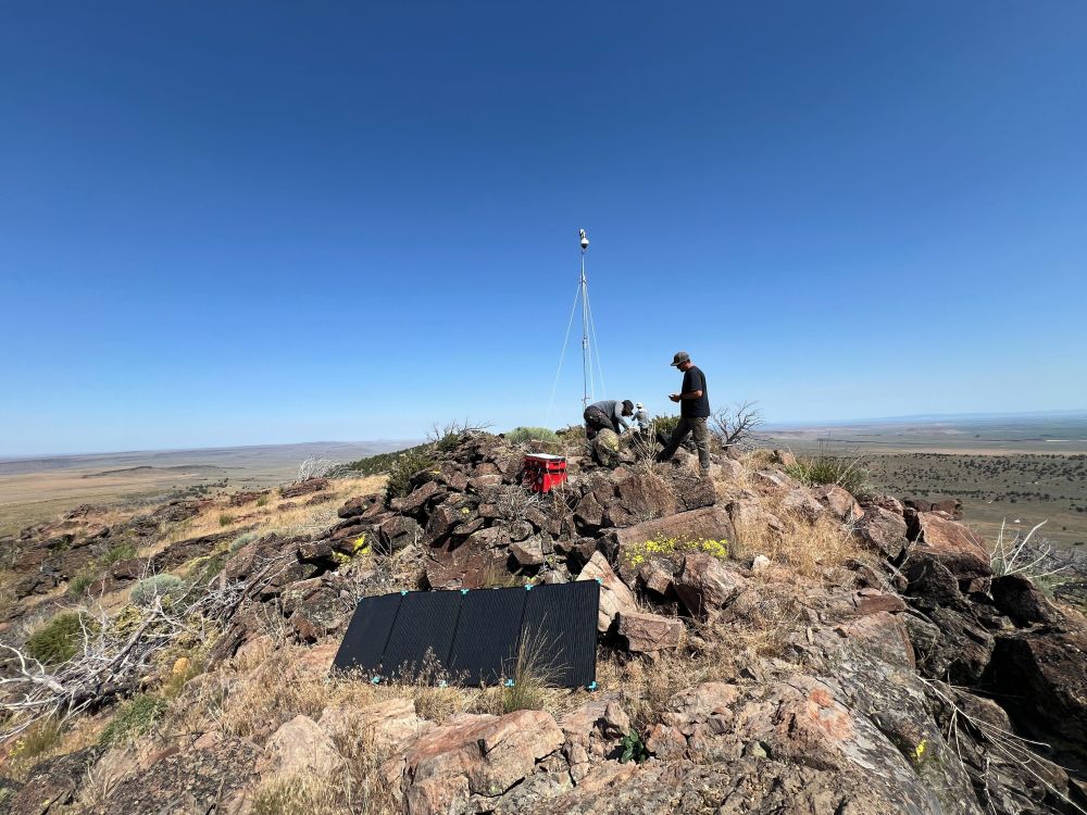 Three men set up a wildfire detection camera on a desert mountaintop.