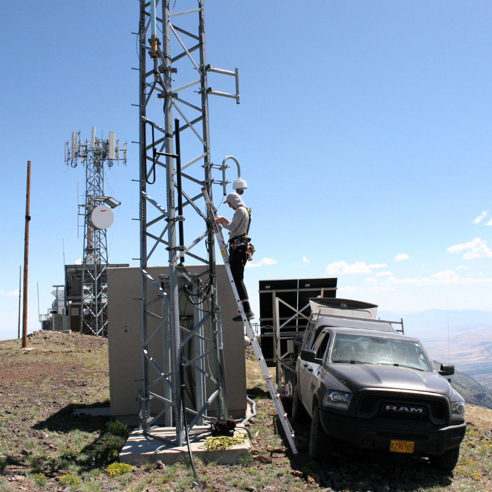 A young man repairs a wildfire camera on a desert mountaintop.