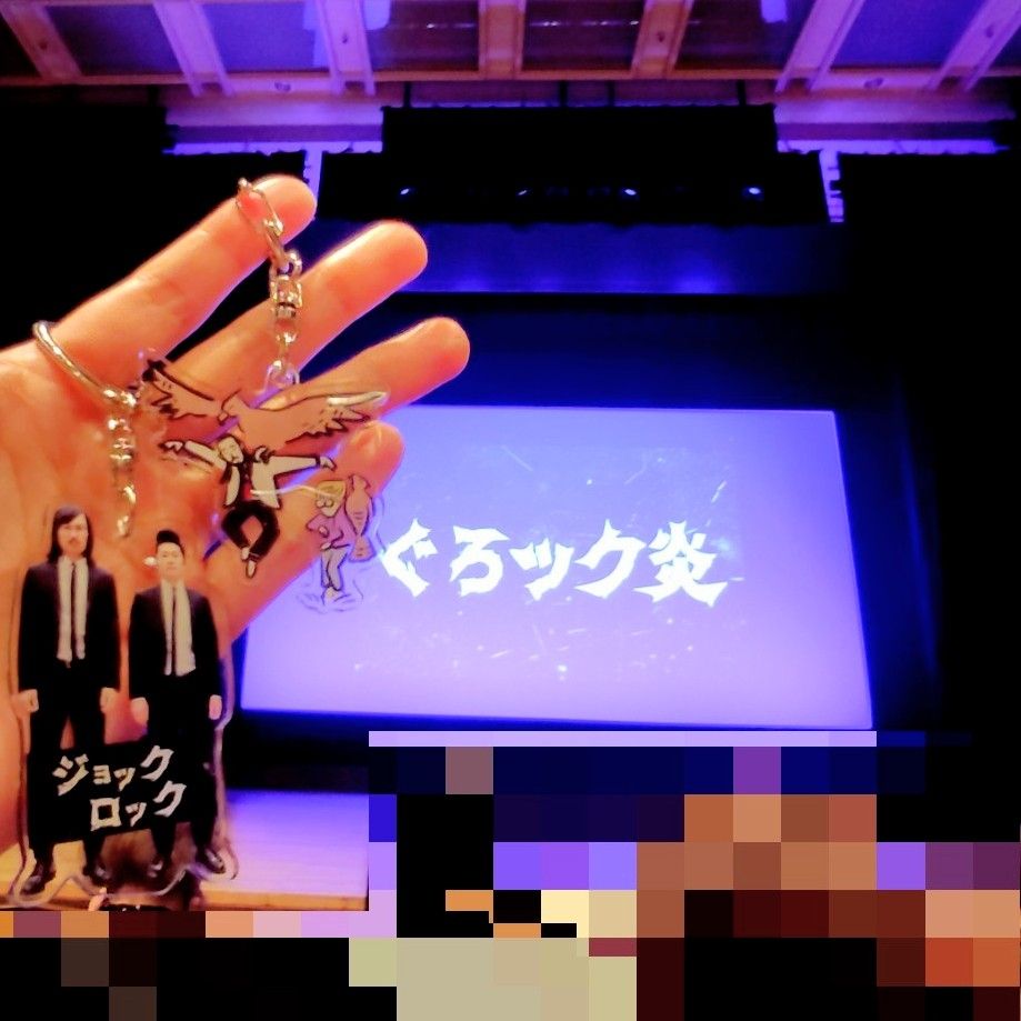 開演前のスクリーンに映る「ぐろック炎」のロゴの前にアクキーを掲げて撮った写真