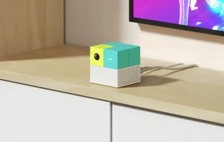 A shot of the Nex Playground console on top of a wooden surface. The console is a small cube shape, with a green coloured top and a motion sensing camera taking up the top left.