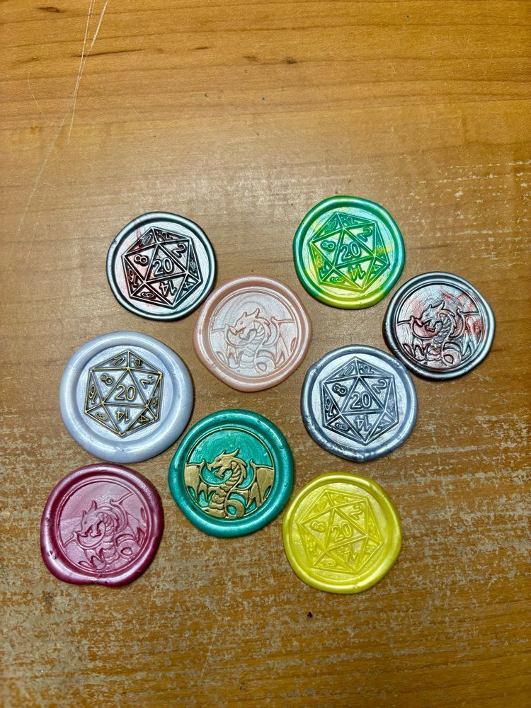 Nine wax seals in various colors. They feature D20s and dragons. 