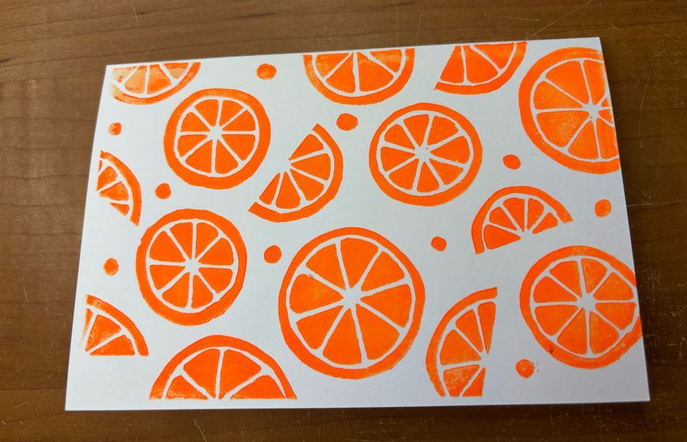 A white card with a lino cut print of orange slices and polka dots