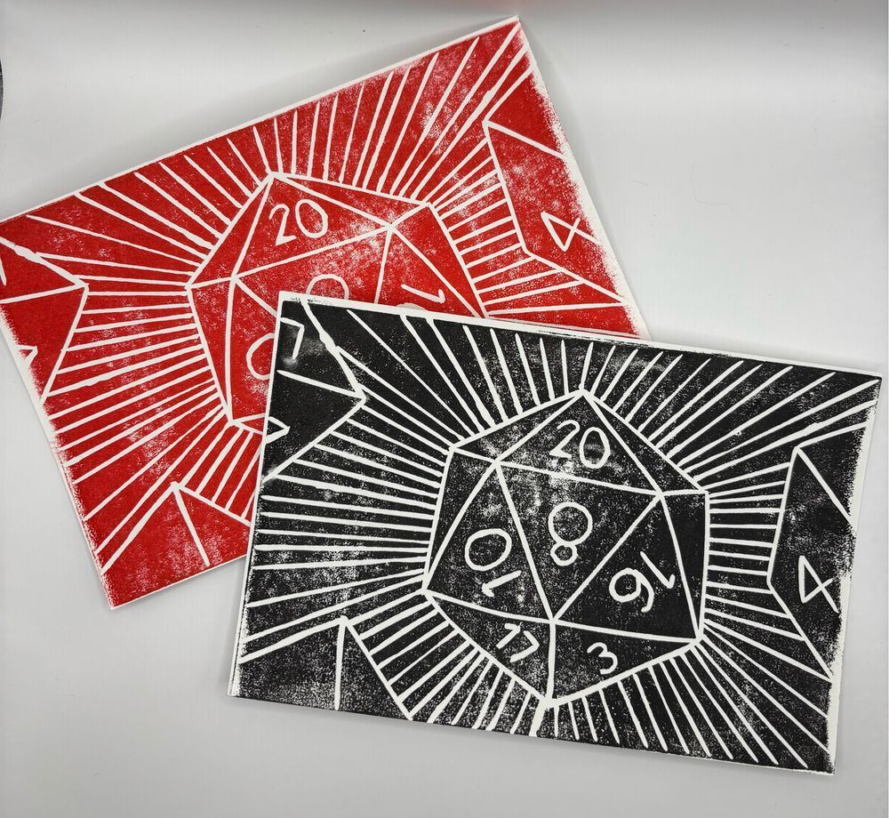 Two linocut postcards featuring a D20. The top one is black, and the one in the back is red. 