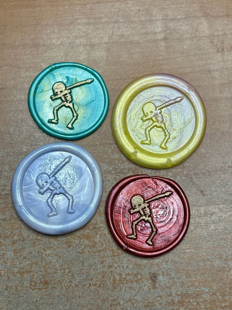 Four wax seals, each in a different color. Each wax seal has an image of a skeleton doing the dab dance move. 