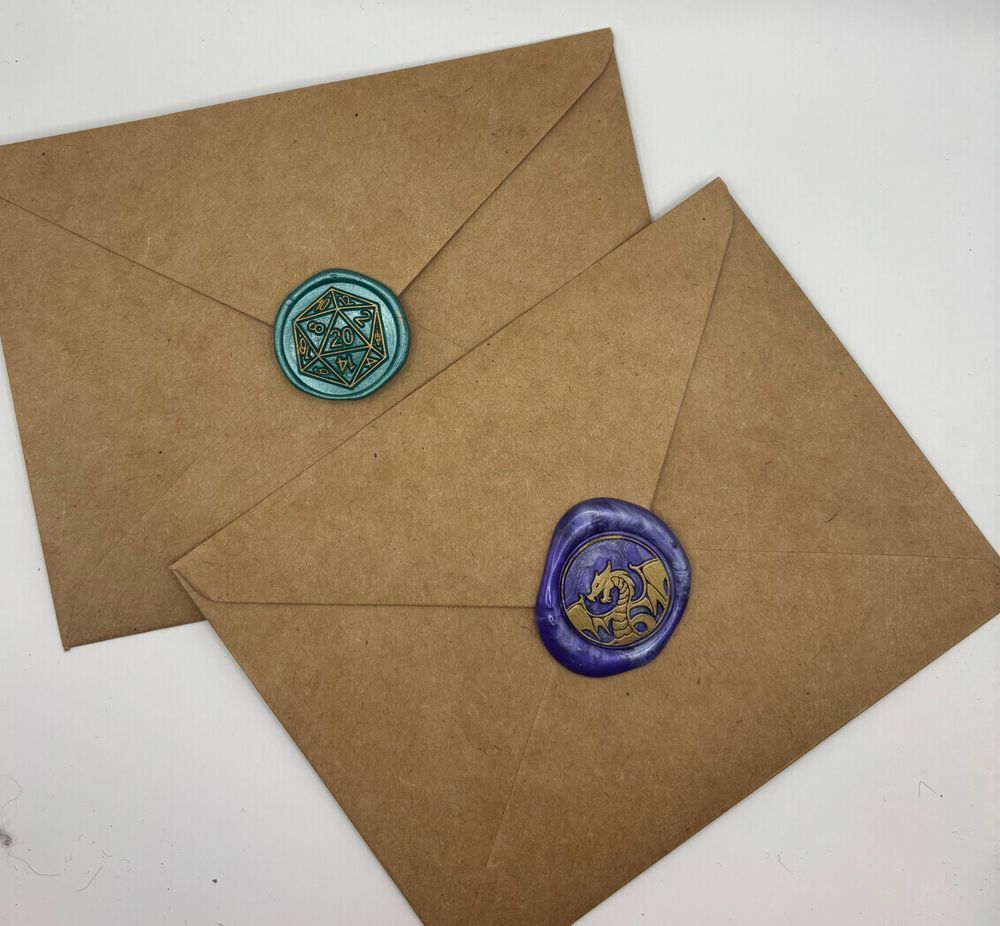 Two envelopes backs sealed with wax seals. One has a teal d20 highlighted in gold and the other is purple with a golden dragon. 