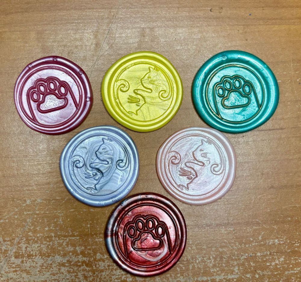 Six wax seals in varying colors. Three are a yin yang design with two cats curling into one another. Three are a cat paw.