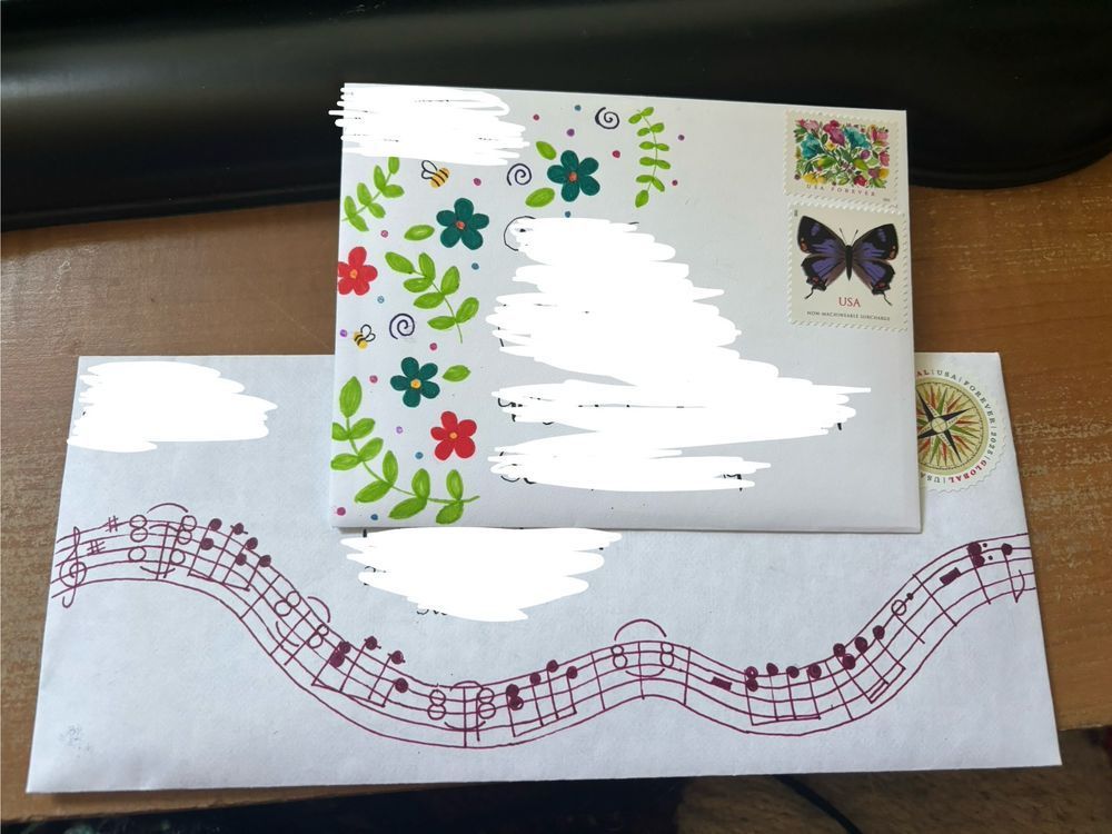 Two envelopes. The first has a pattern of leaves, pink and blue flowers, and bees. The second has a music staff with a Bryan Adams song written out on it. 
