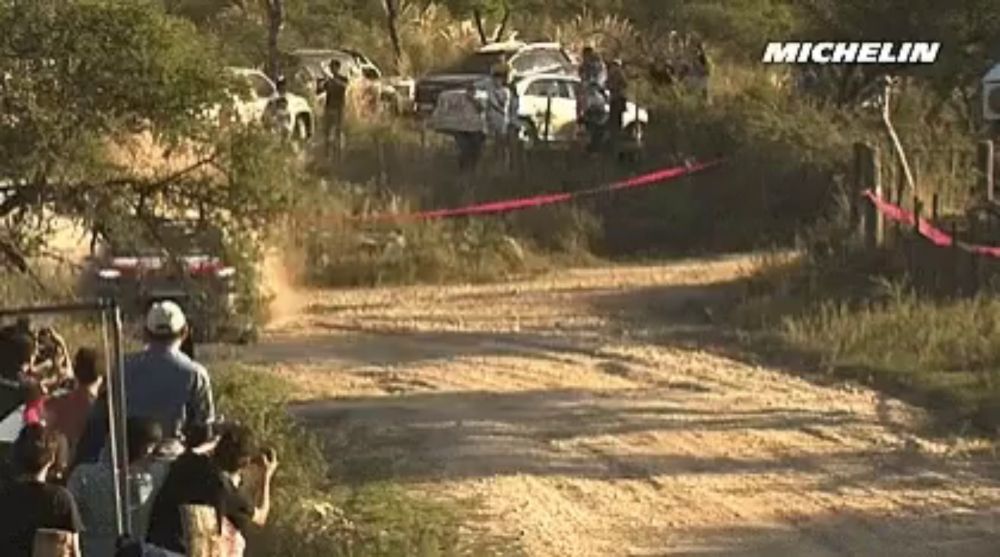 a group of people are watching a car race on a dirt road with michelin written on the bottom