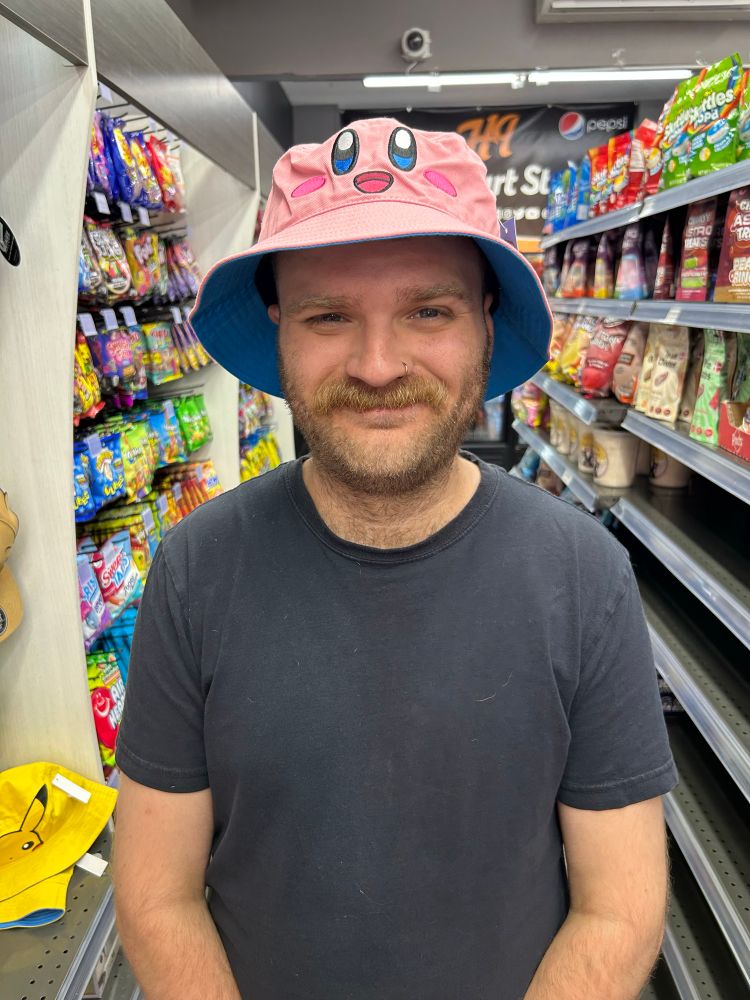Scruffy man with a moustache and beard wearing a black t shirt and a Kirby bucket hat